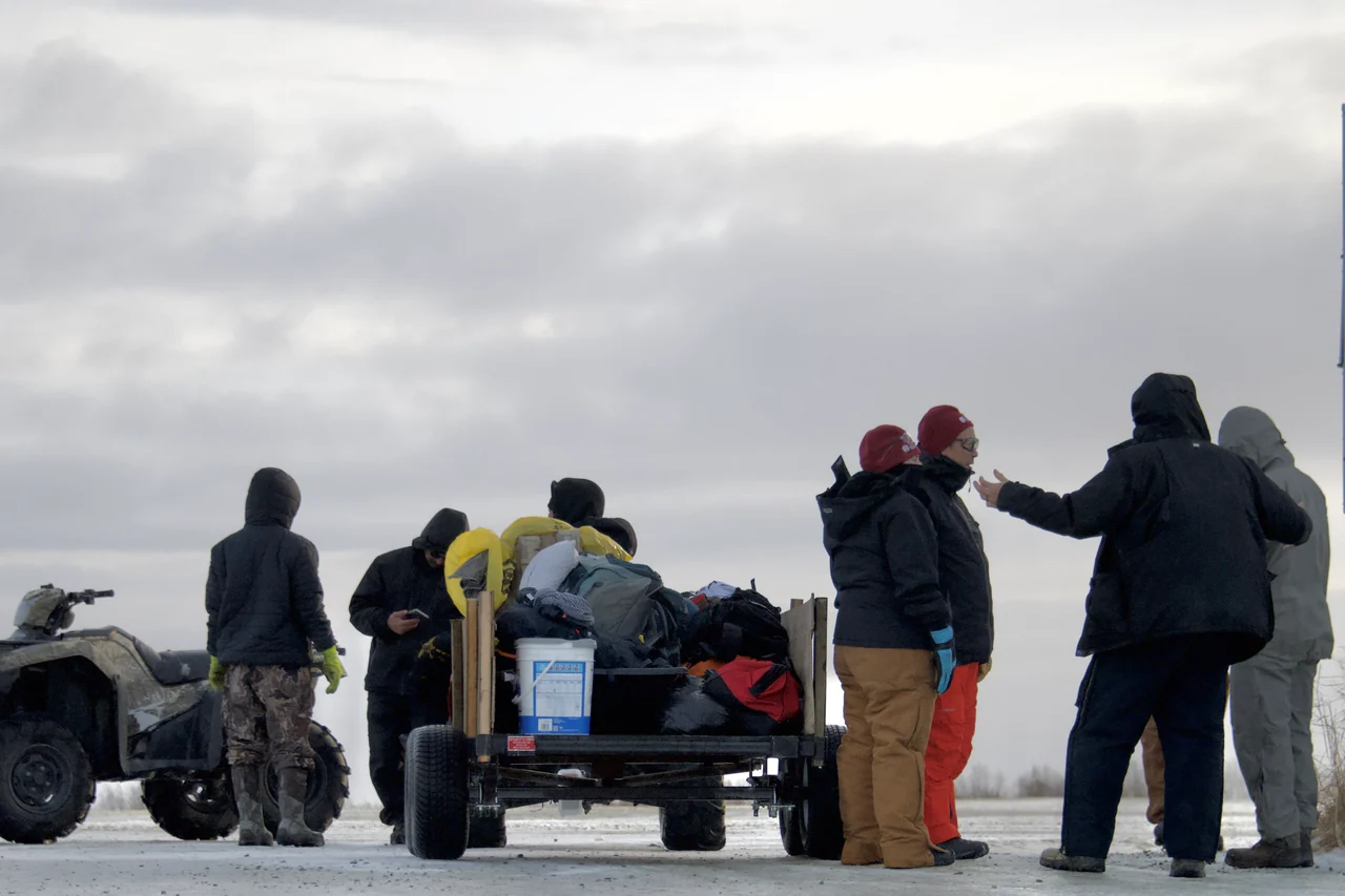 People gather beside a loaded trailer and an all-terrain vehicle in the snow.