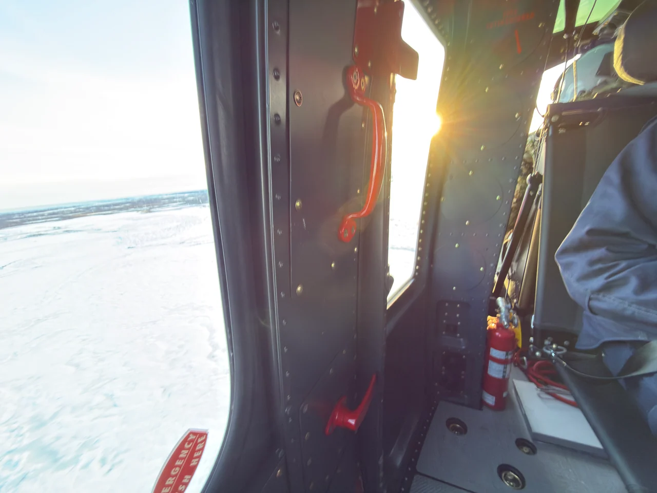 Sunlight enters a helicopter cabin above a snow-covered landscape.