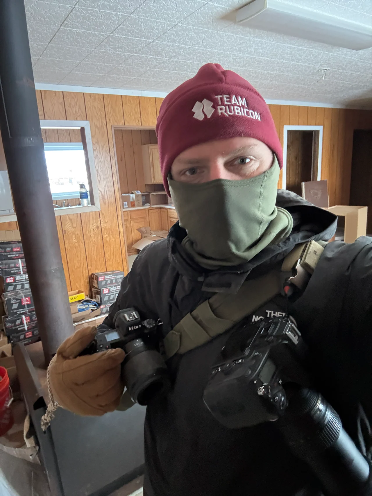 Josh Walker wears a Team Rubicon hat, face covering and camera harness indoors.