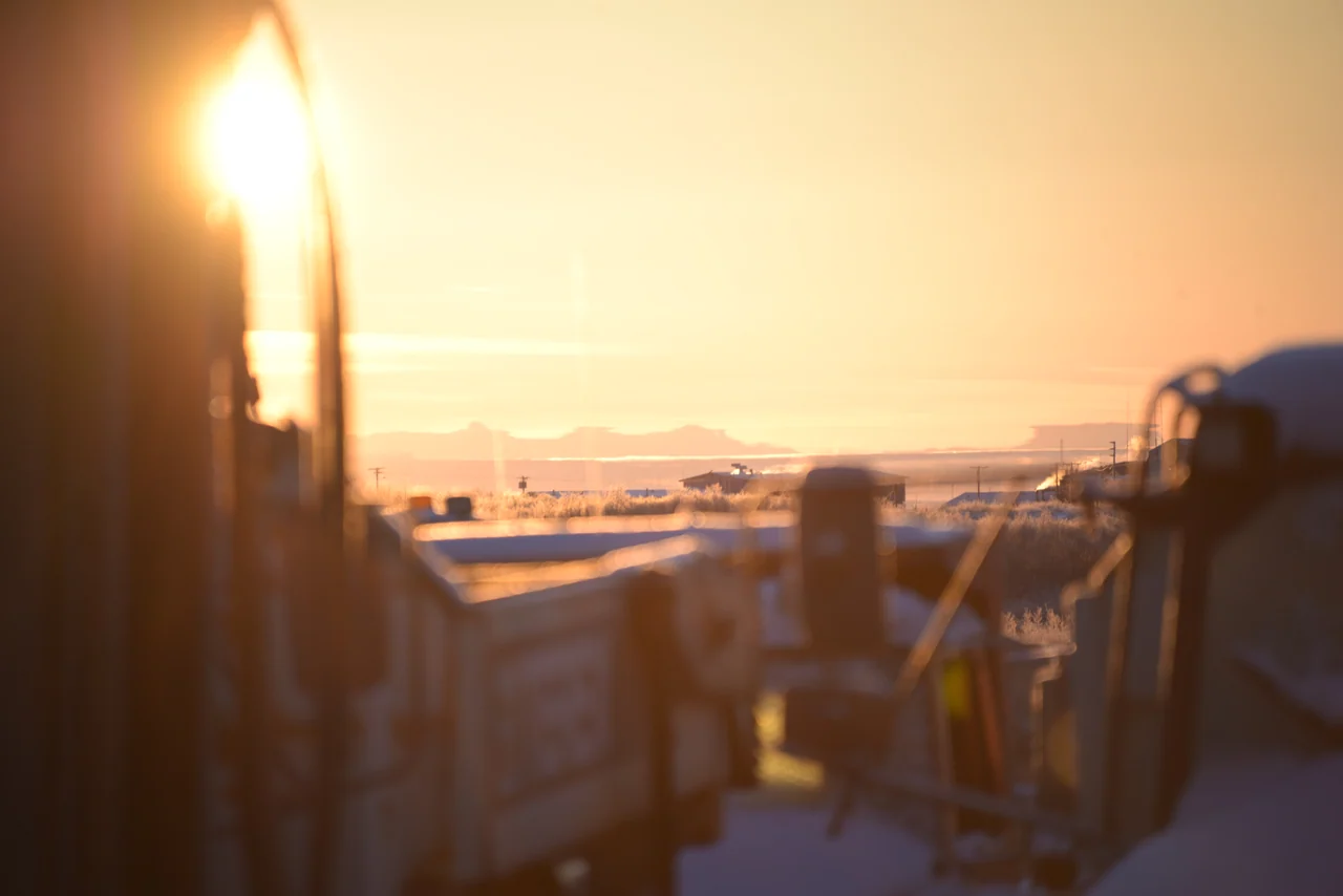 Low golden sunlight falls across a snow-covered settlement beyond a porch.