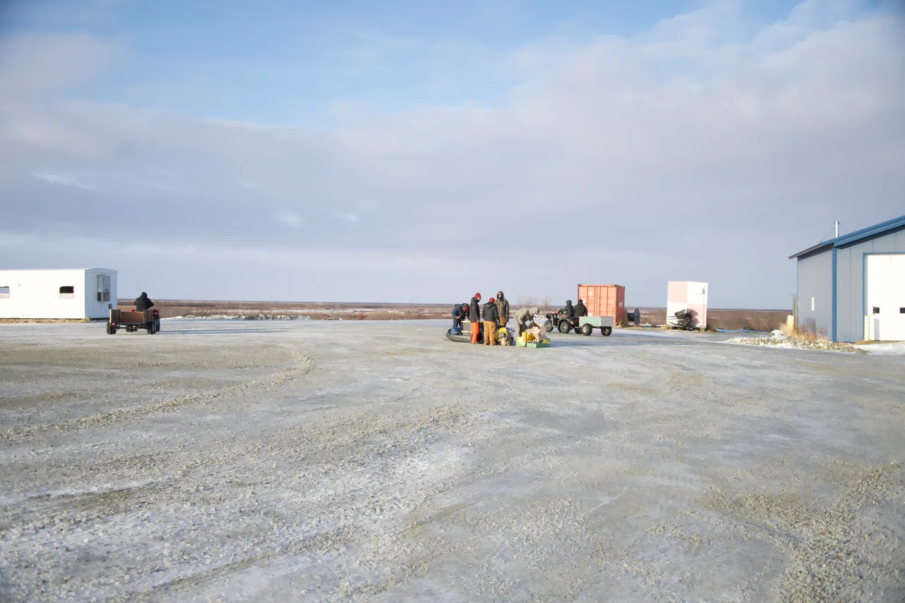 A small group stands with equipment on a broad gravel airfield.