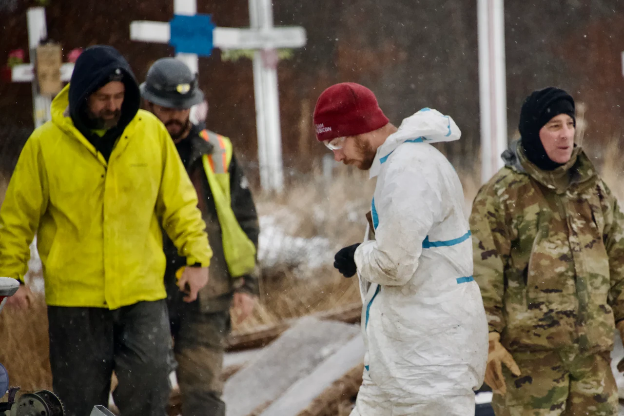 Volunteers in cold-weather and protective clothing stand together beside building materials.